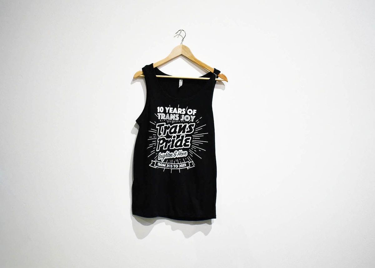 A black tank top hangs on a wooden hanger, featuring "Trans Pride Brighton & Hove".