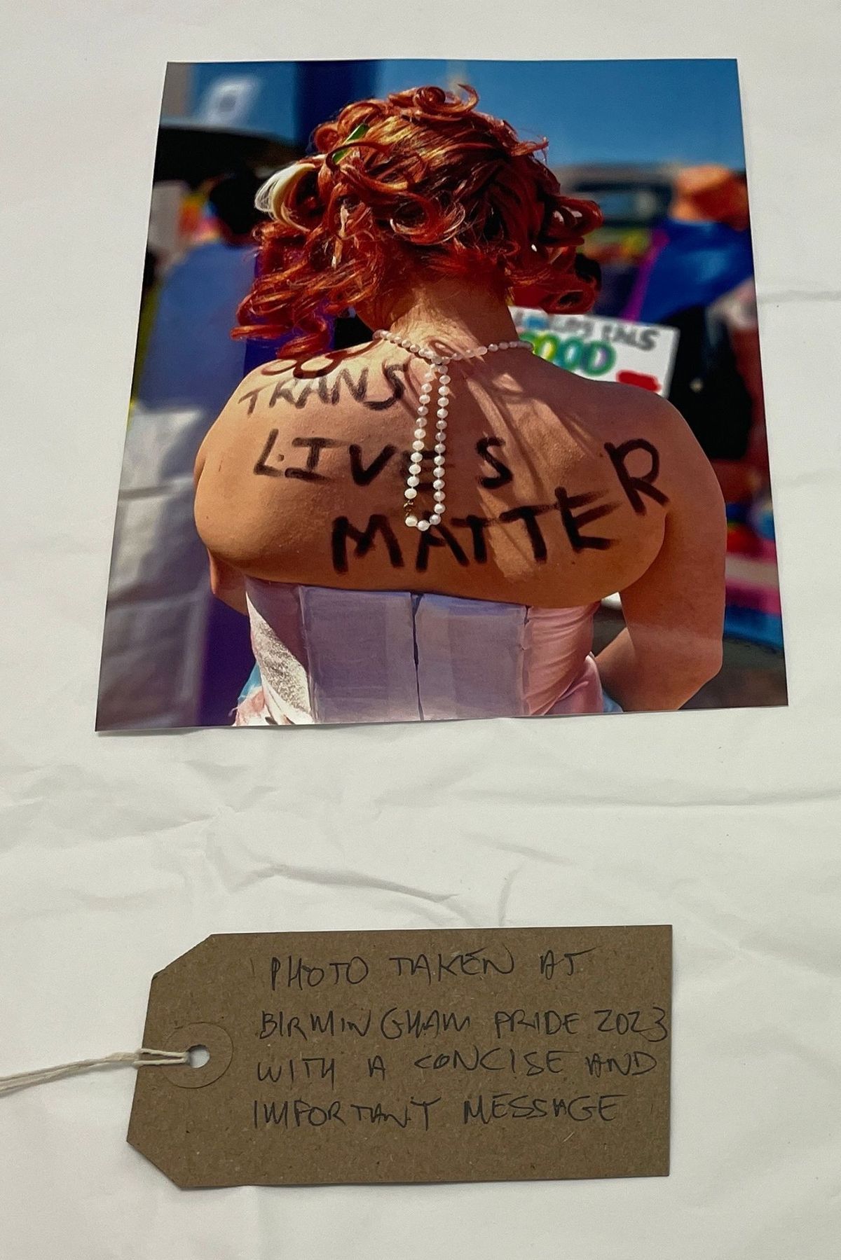 The image shows a person from the back wearing a pearl necklace, with "Trans Lives Matter" written across their back.