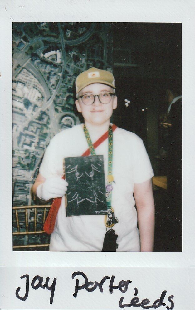 A person wearing glasses holds a black and white drawing while smiling at the camera.