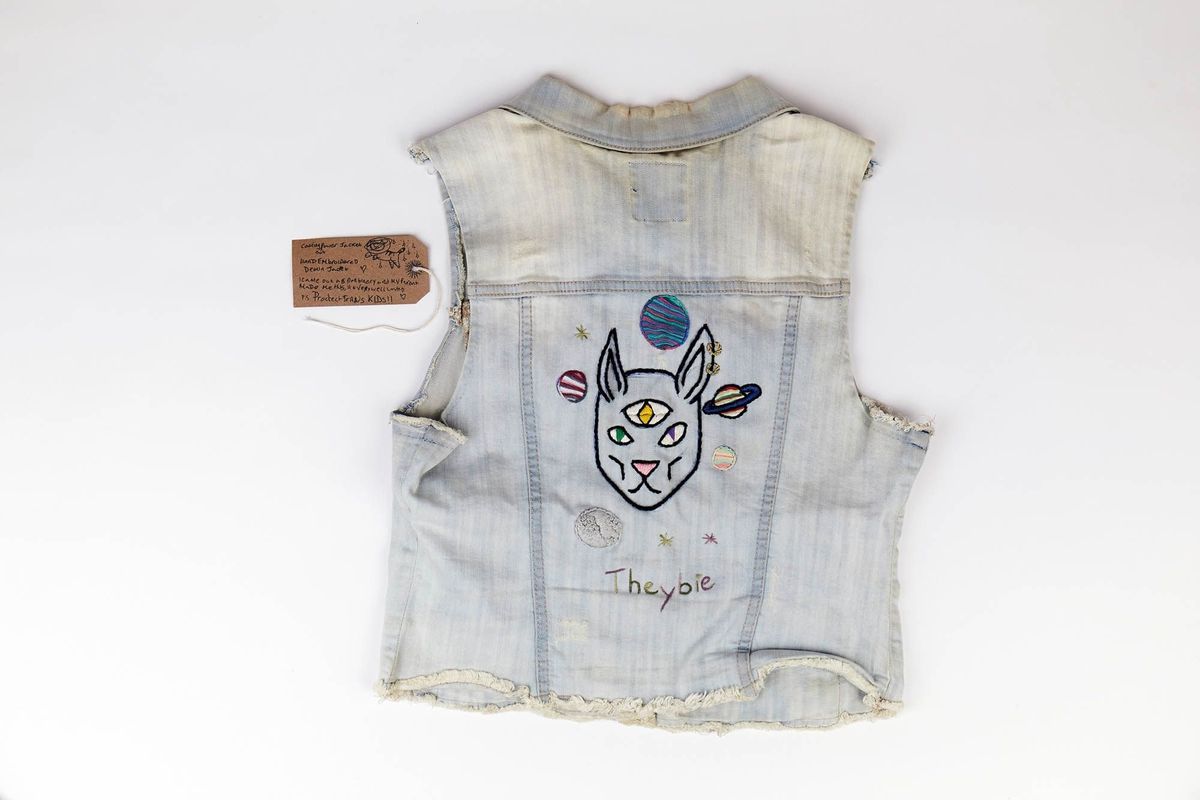 A denim vest displays a colorful embroidered design featuring planets and a unique animal face.