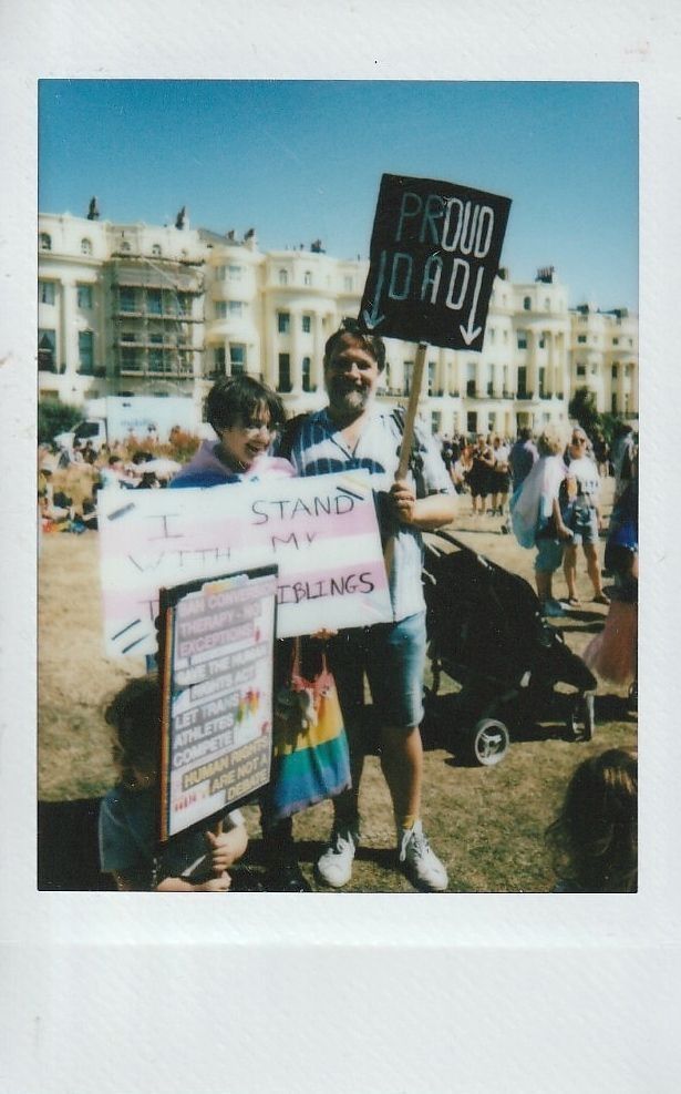 Three people stood holding signs, one of which says 'Proud Dad'.