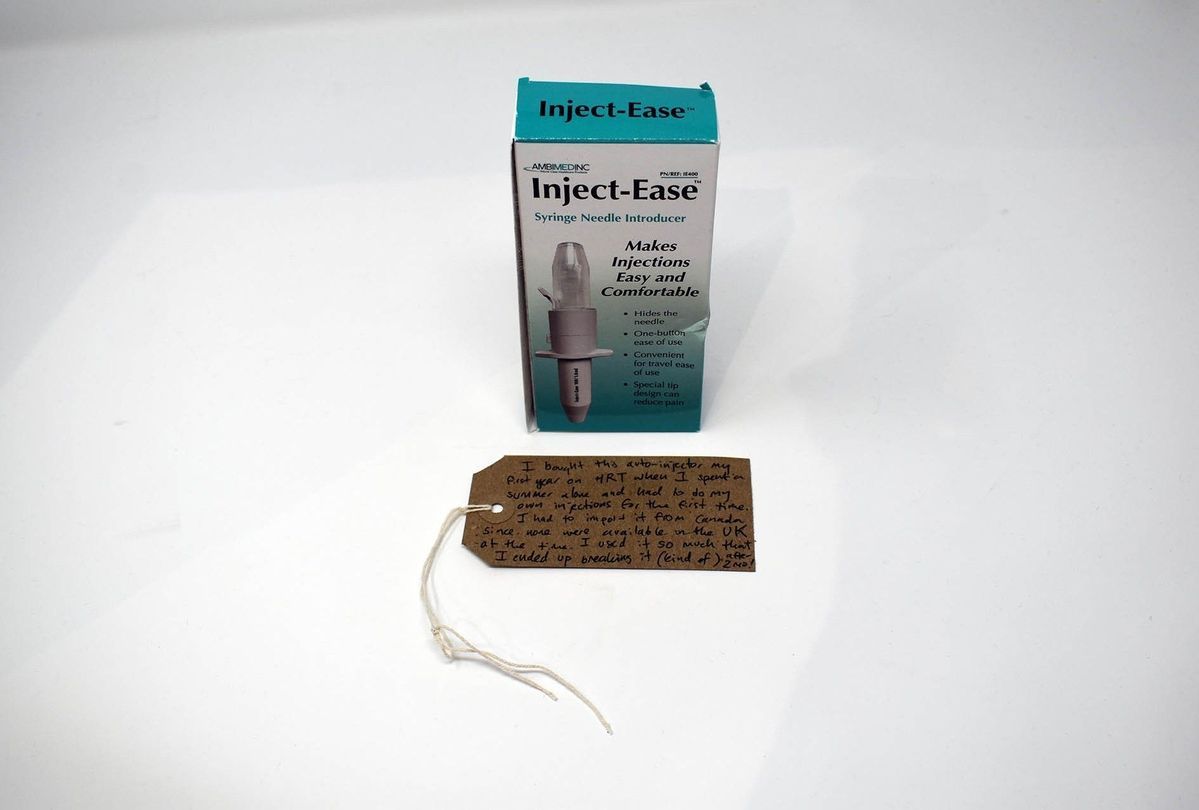A box of Inject-Ease which is turquoise and white with a photograph of the syringe needle introducer on it. Underneath the box is a brown tag with writing on it.