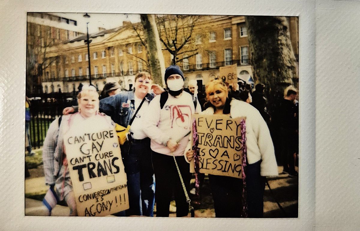 A group of people proudly hold signs which say "CAN'T CURE GAY CAN'T CURE TRANS CONVERSION THERAPY IS AGONY" and "EVERY TRANS IS A BLESSING".