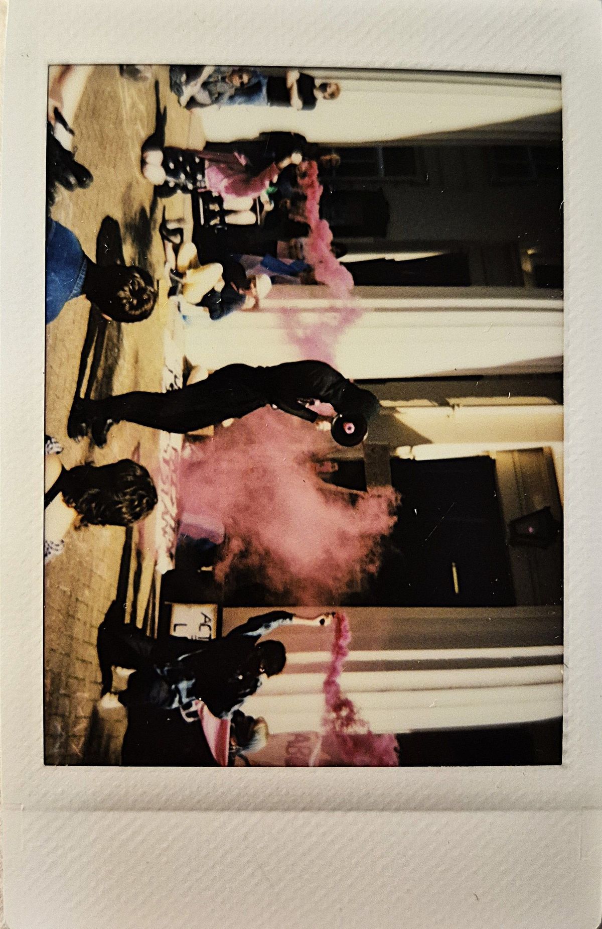 A group of people gather outside a building as pink smoke fills the air.