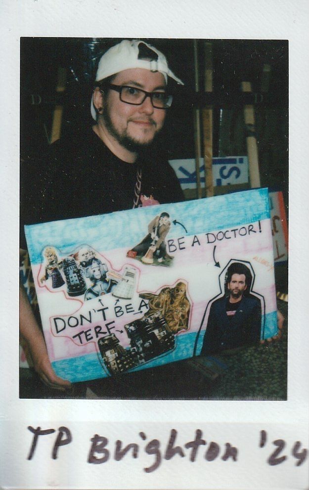 A person wearing a cap and glasses holds a colorful collage poster with various images and text.