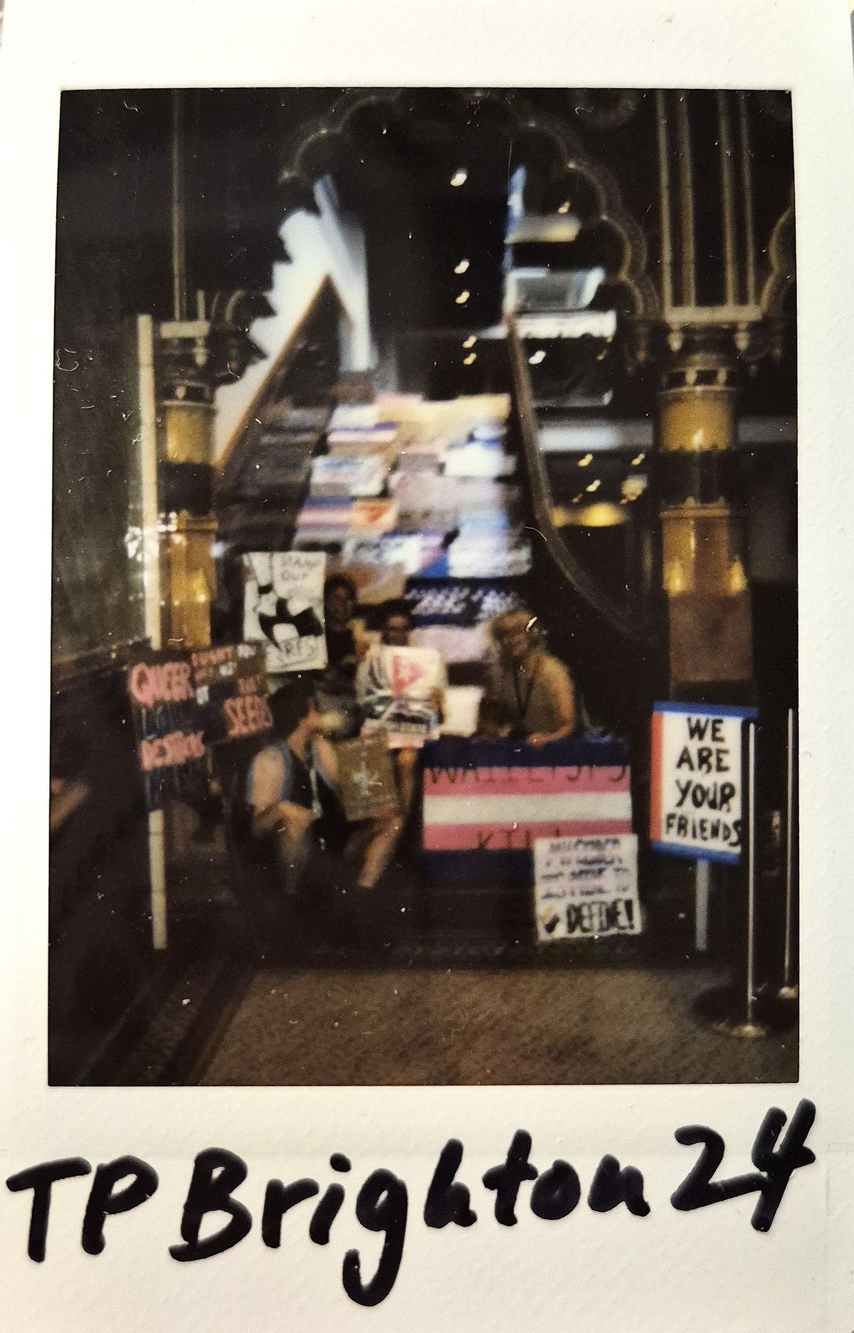 A group of people holding various signs sits on steps inside a building under ornate arches.