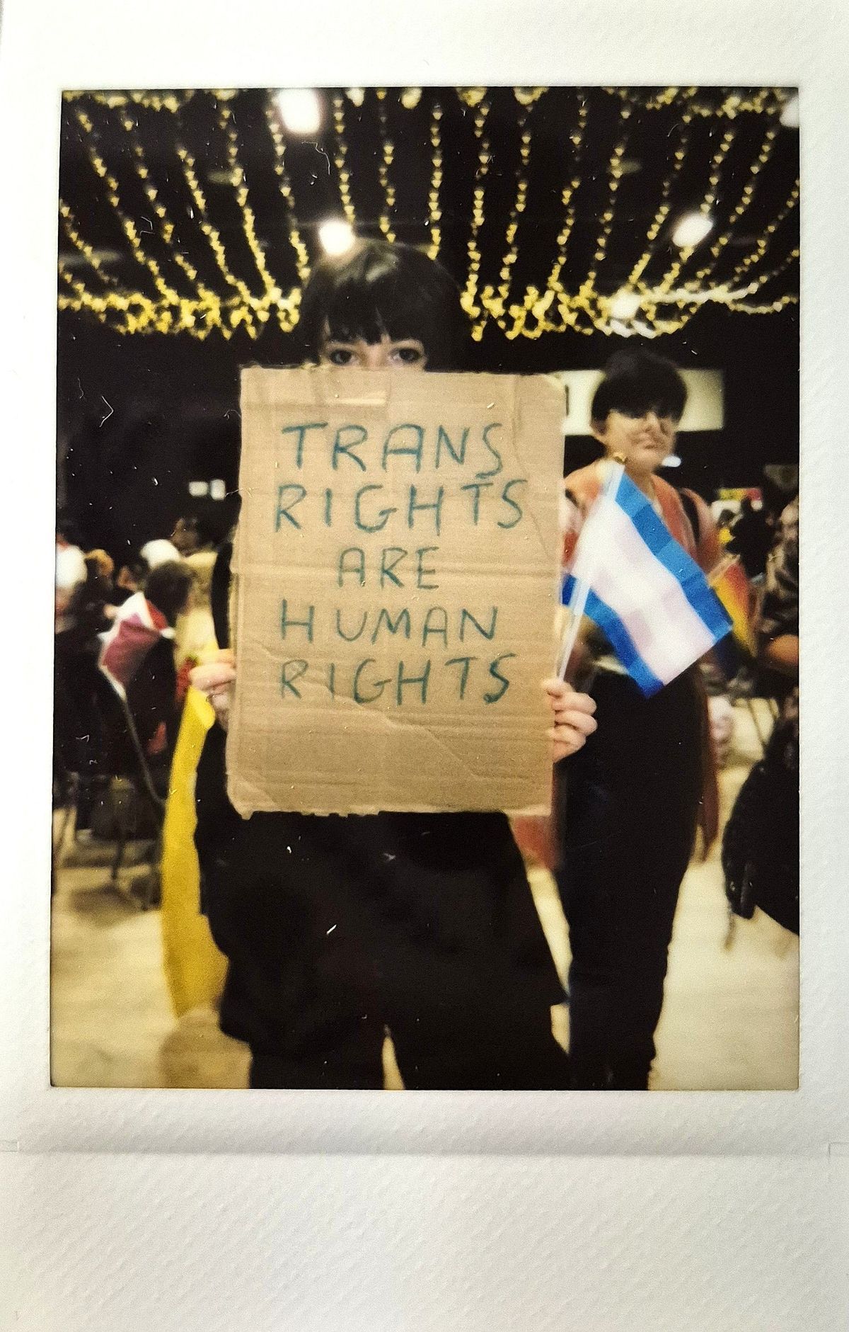 A person holds a sign saying "Trans Rights Are Human Rights" while holding a trans flag.