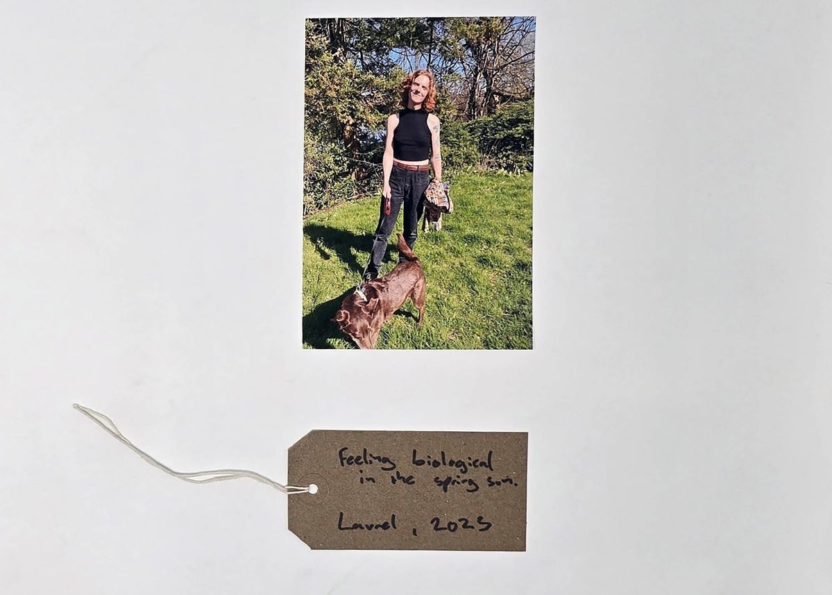 Photo of a red haired person holding a dog on a lead in a garden. With a brown, handwritten luggage tag.