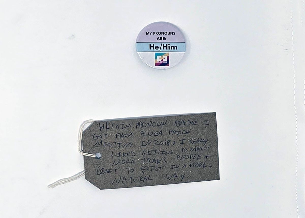 A "He/Him" pronoun badge from a 2018 pride meeting with a brown tag.