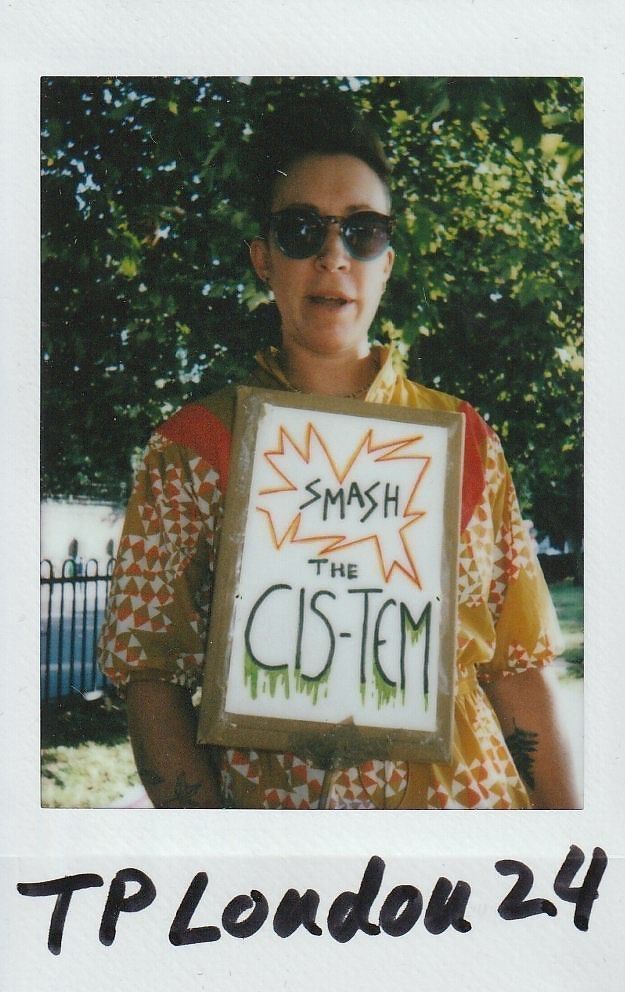 A person wearing sunglasses holds a sign with “Smash the CIS-TEM” written on it.