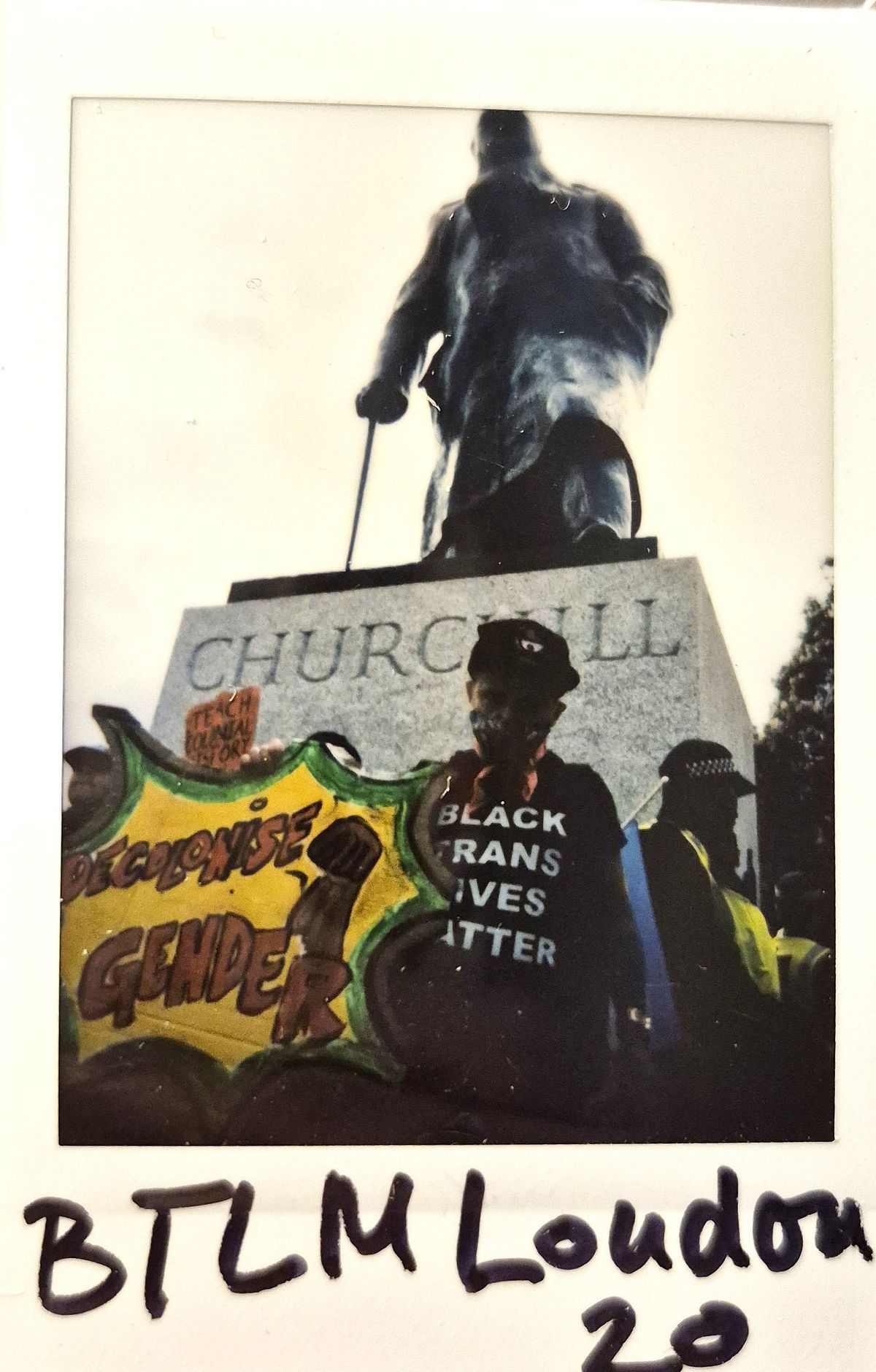 A person stands with a sign and shirt in front of a Churchill statue.