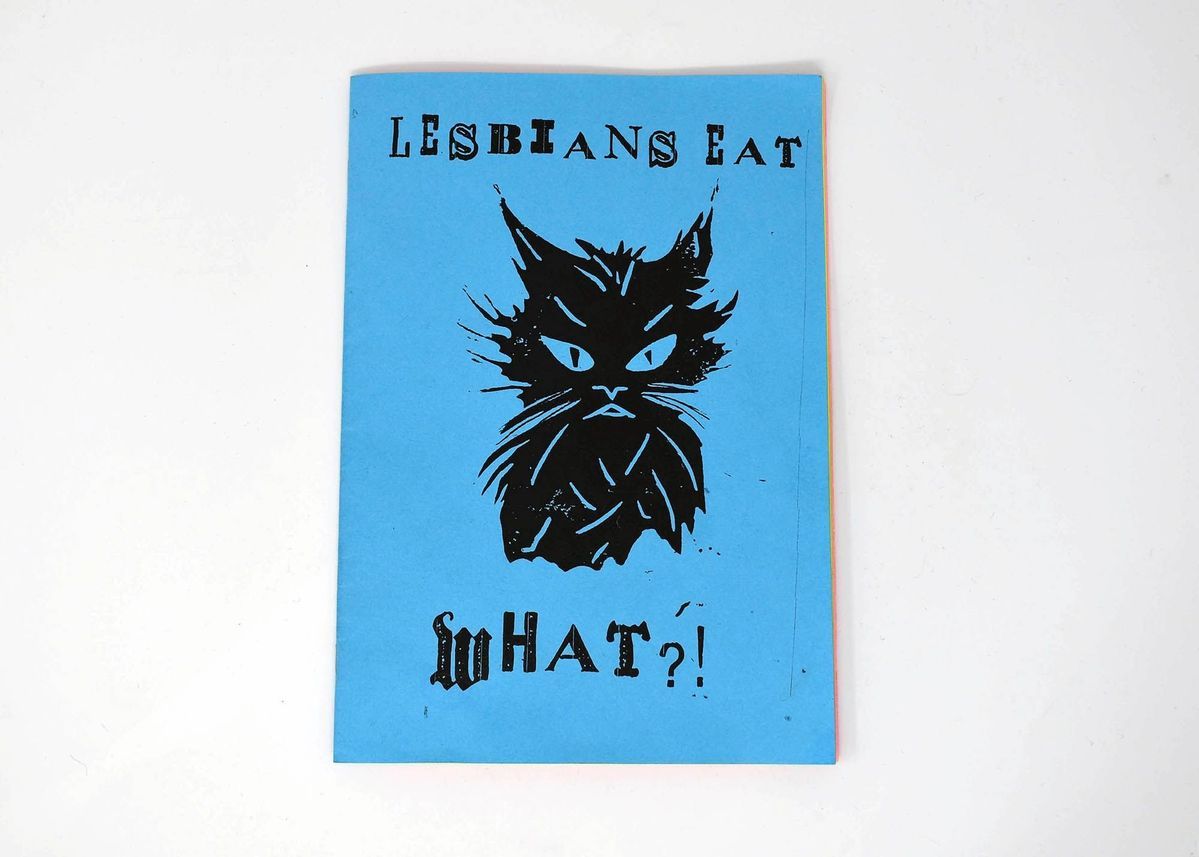 The image shows a blue booklet with a black cat illustration and text saying "Lesbians Eat What?"