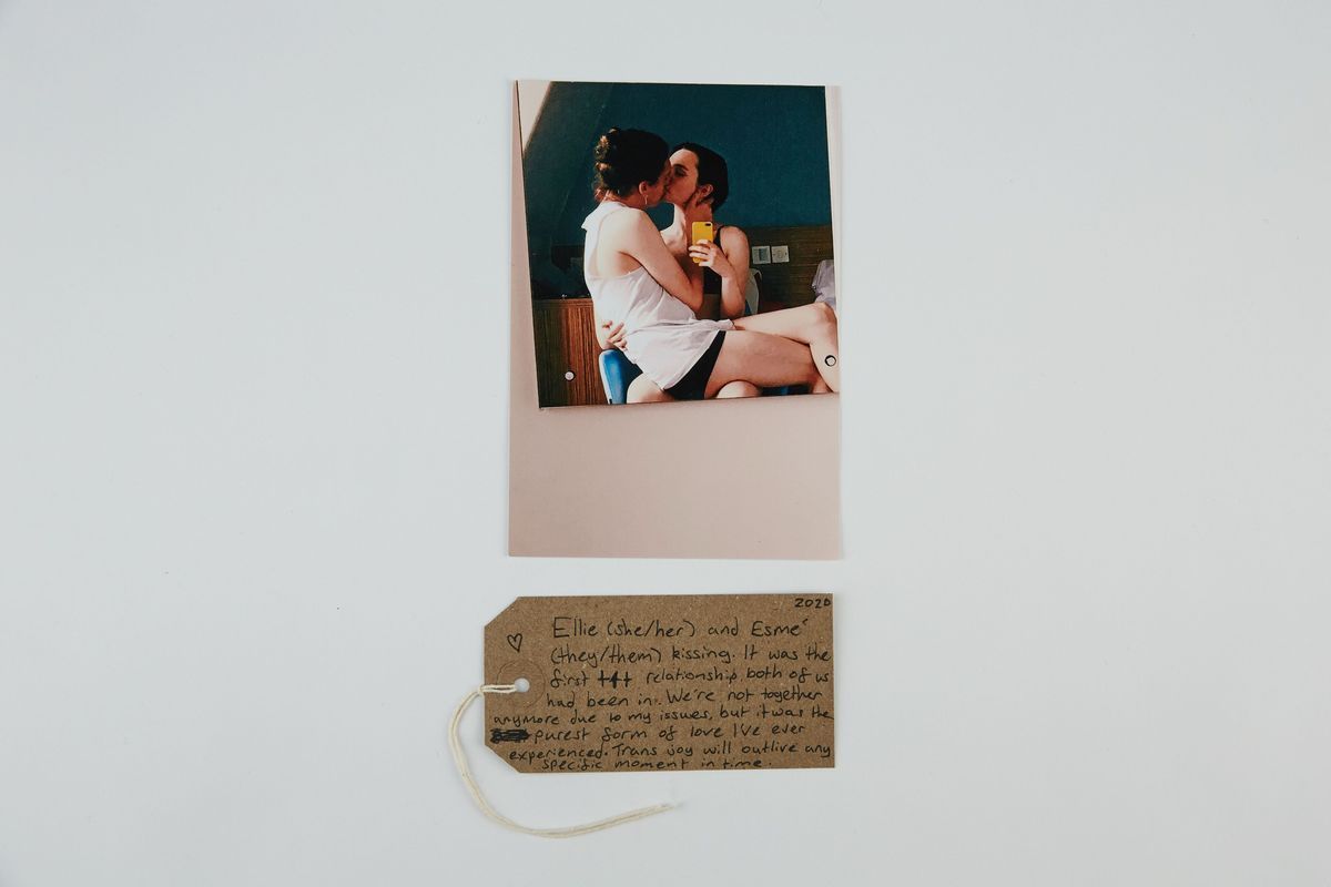 Photo of two dark haired people, one sitting the the others lap, kissing. With a brown, handwritten luggage tag.
