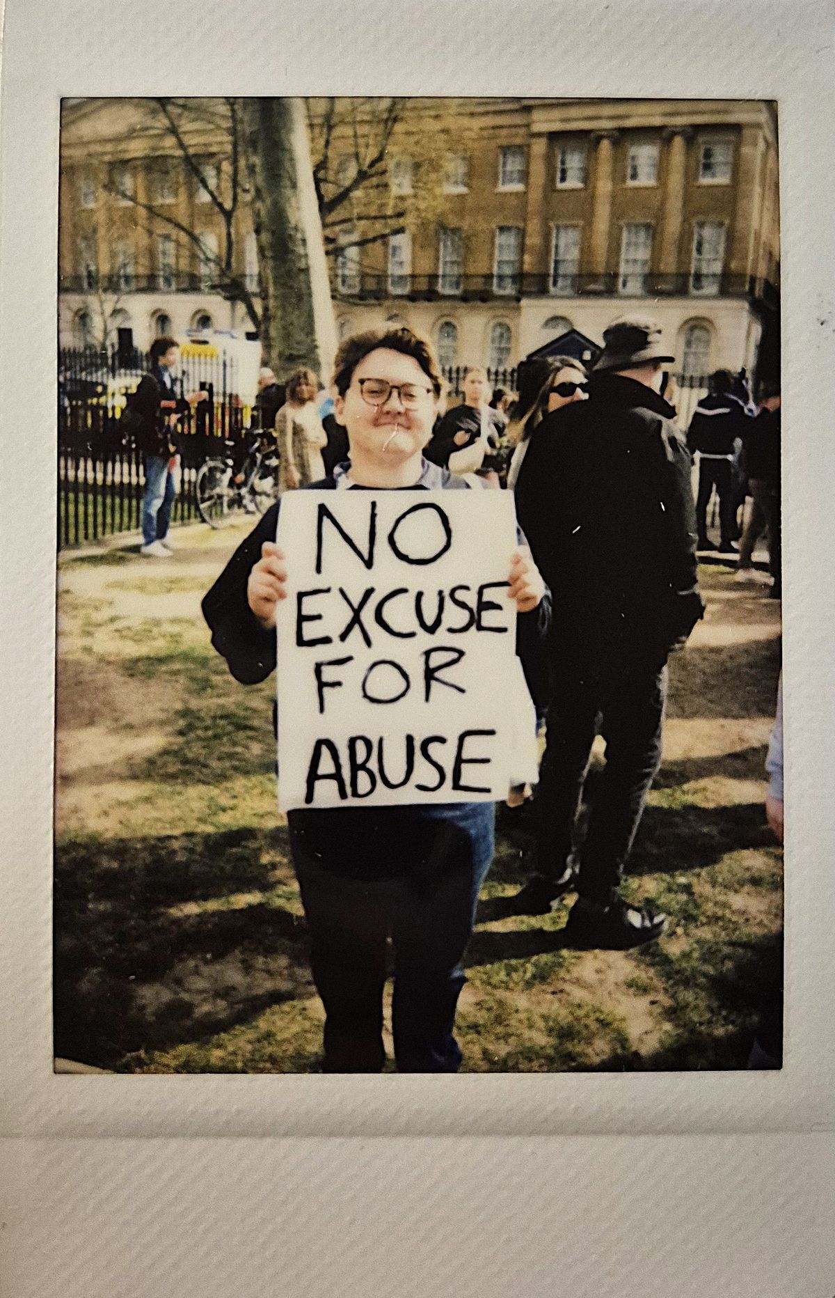 A person holds a sign stating "No Excuse for Abuse" at an outdoor gathering.