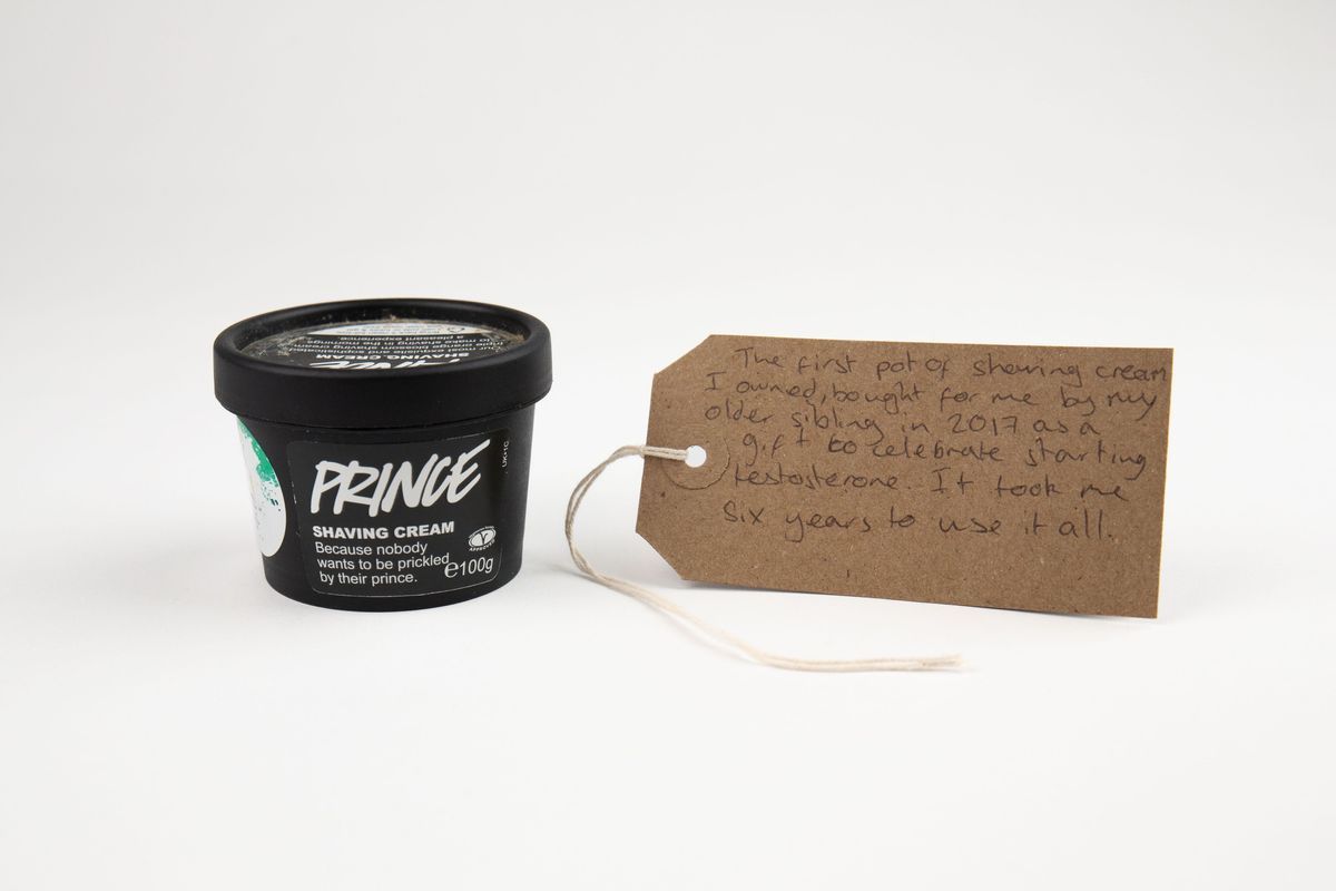 A black tub of 'Prince' Shaving Cream from Lush. There is a brown tag with writing on it next to it.