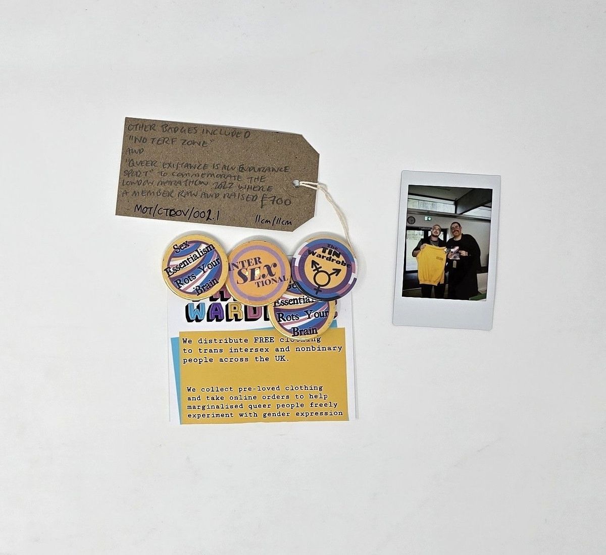 Four Badges Pinned Onto 'The Tin Wardrobe' Card. The badges are all in yellow, blues and purples and are of 'Sex Essentialism Rots Your Brain' x2, 'Inter SEX Tional', 'The Tin Wardrobe'.
