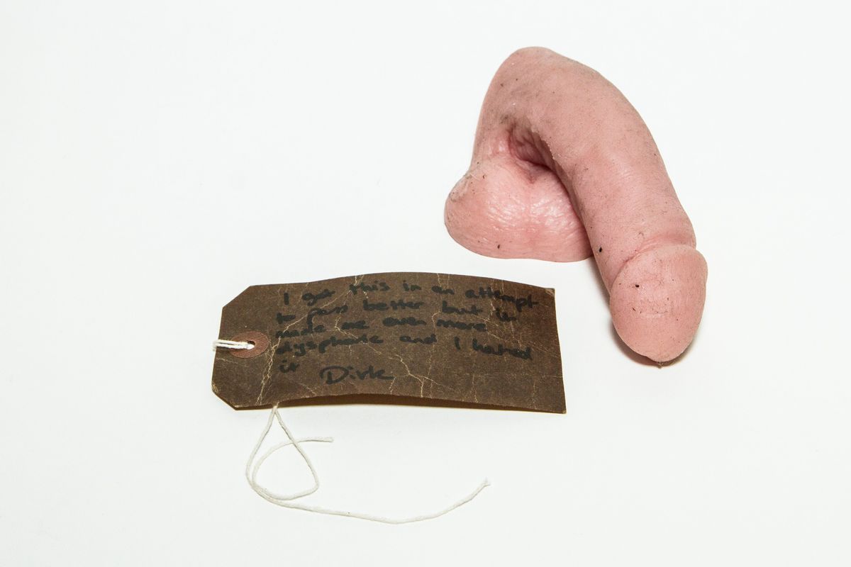 Prosthetic penis & testicles (packer); made of silicone, pink, moulded with lifelike detail of skin wrinkles, hair follicles etc. Flat surface across base with moulded concave indent in centre.