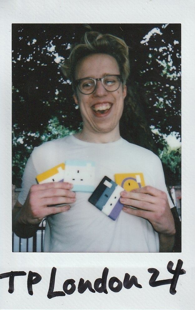 A person wearing glasses smiles broadly while holding colorful plug sockets outdoors.