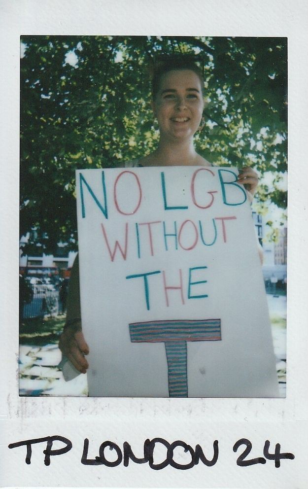 A person smiles while holding a sign reading, "No LGB Without the T," in a park