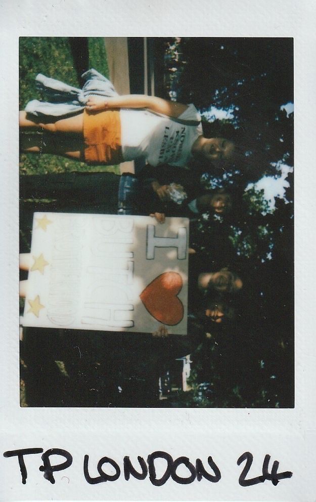 Three people are holding a large sign with love symbolism, standing outdoors on a sunny day.