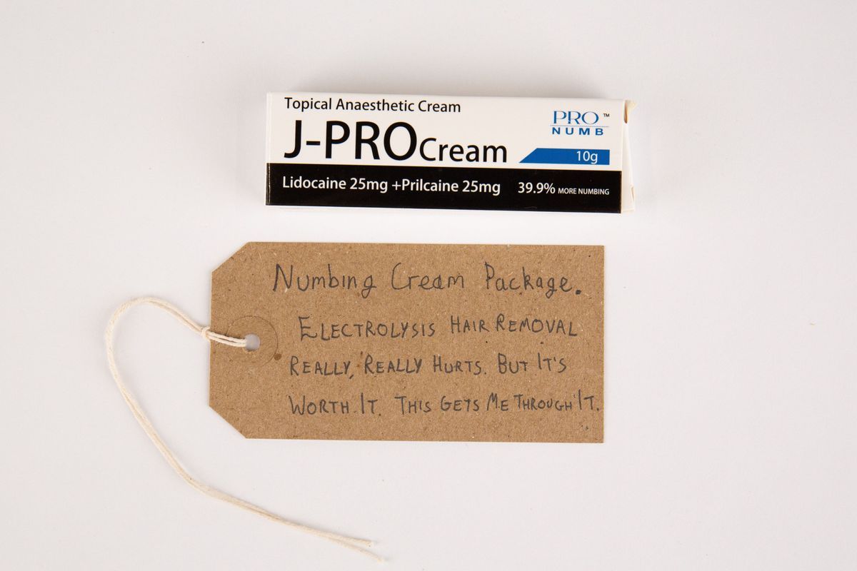 White, black and blue Box of J-PRO topical anesthetic cream. With a brown, handwritten luggage tag.