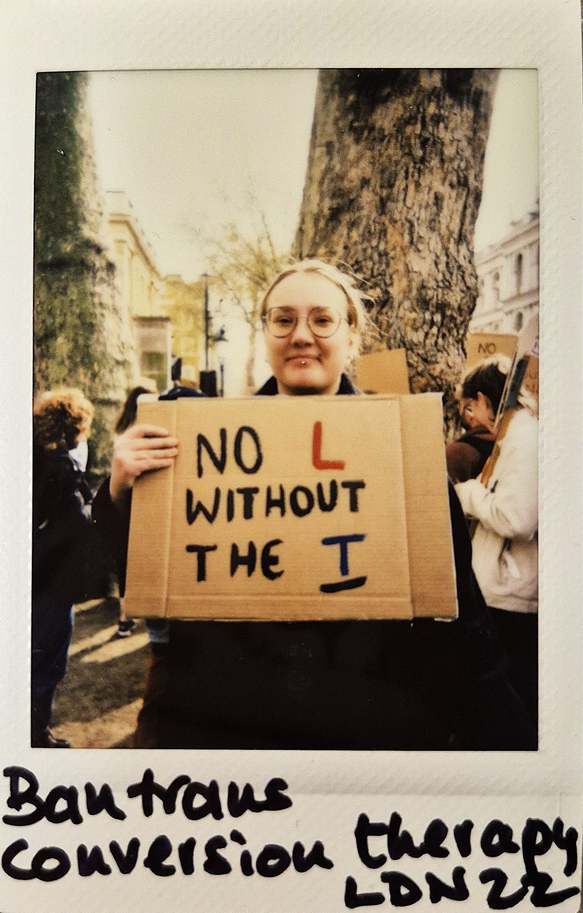 A person is holding a sign that says "No L without the T" in a protest.