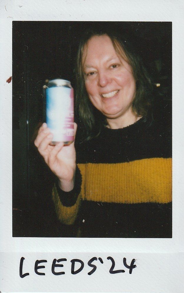 A person wearing a striped sweater is happily holding a colorful can, labeled "LEEDS '24"