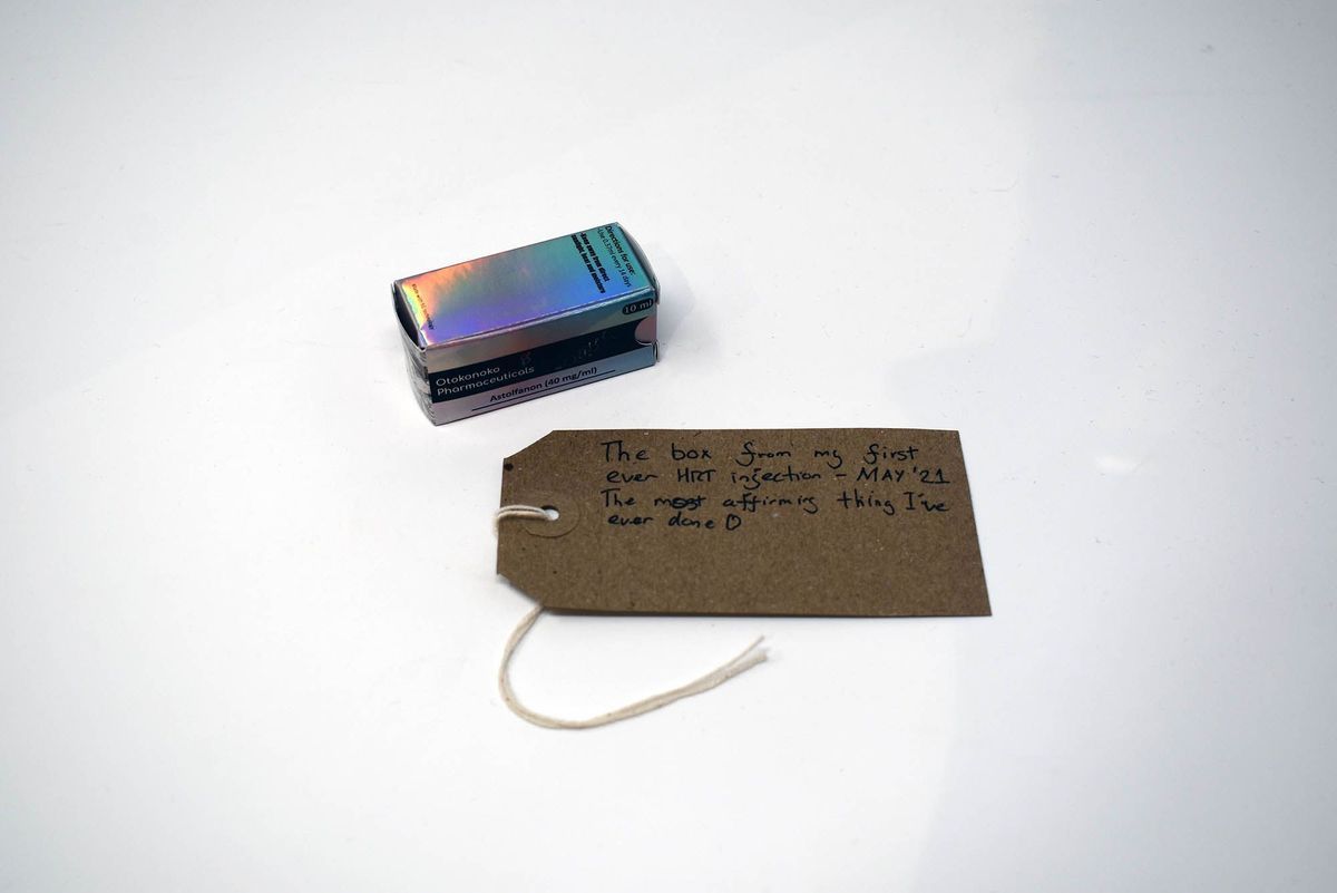 An empty hormone box which is holographic and a brown tag with writing on it next to it.