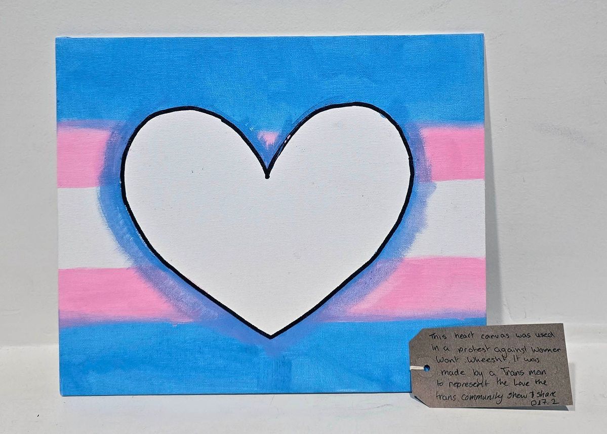 A square placard which is painted in the trans flag and a heart drawn in the middle.