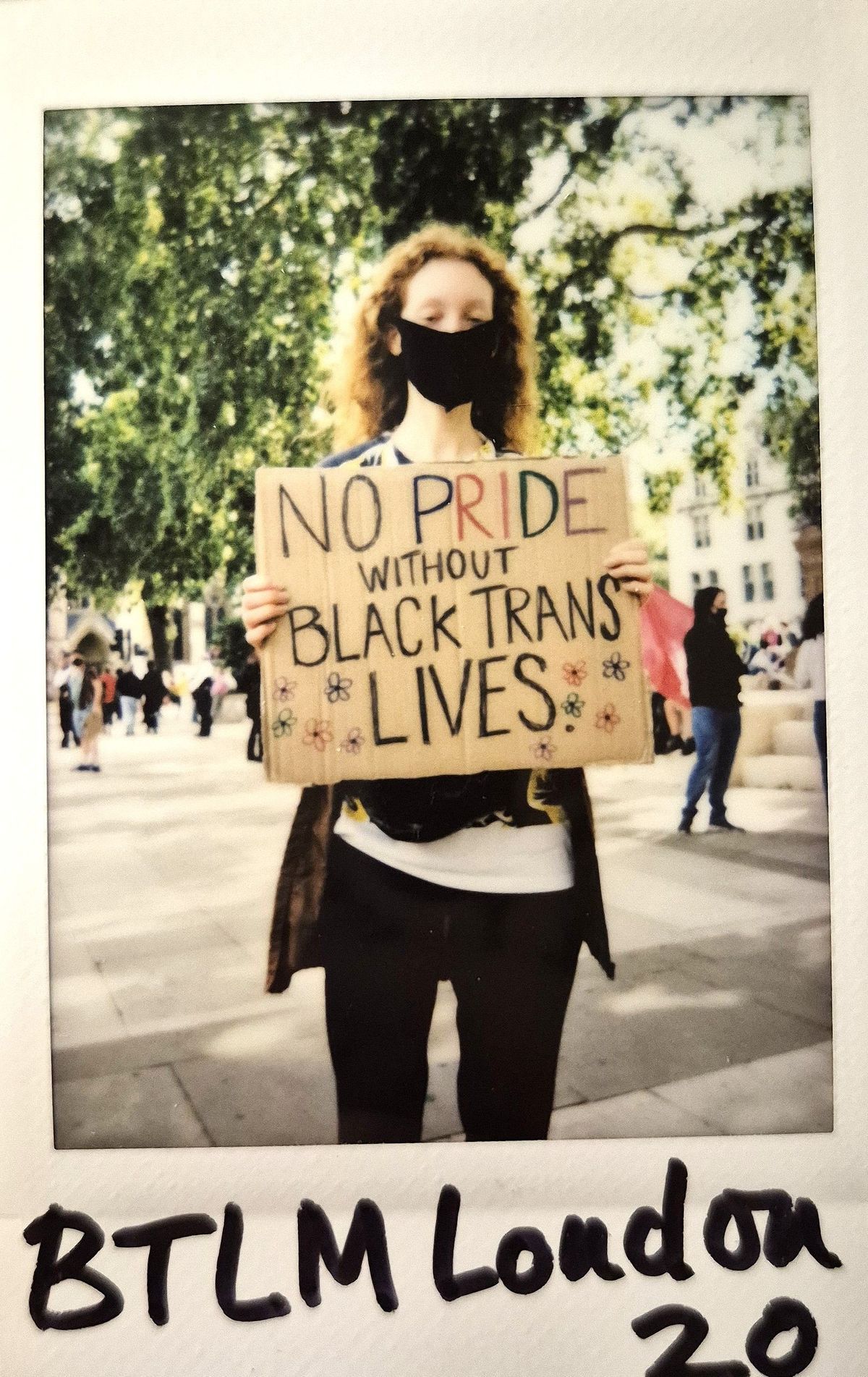 A person stands holding a sign reading "NO PRIDE WITHOUT BLACK TRANS LIVES".