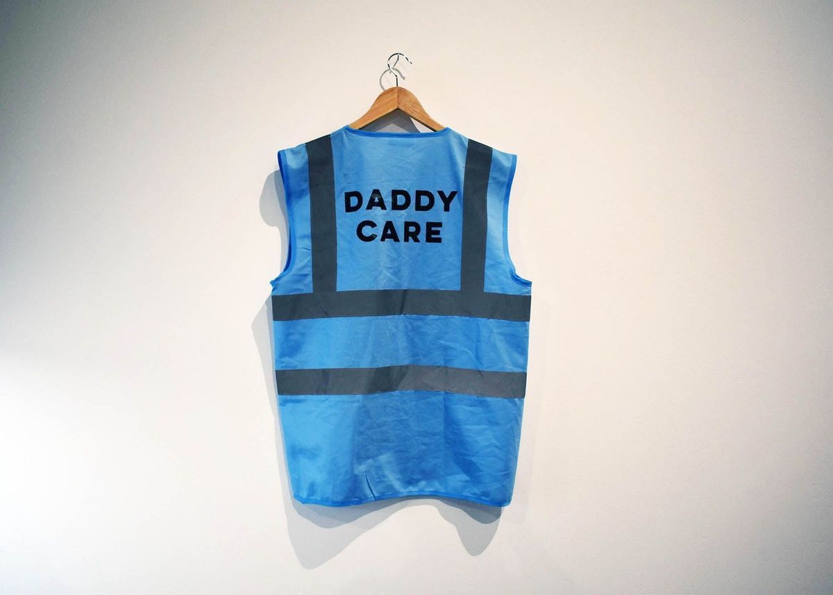 A blue safety vest with "DADDY CARE" hangs on a wooden hanger.