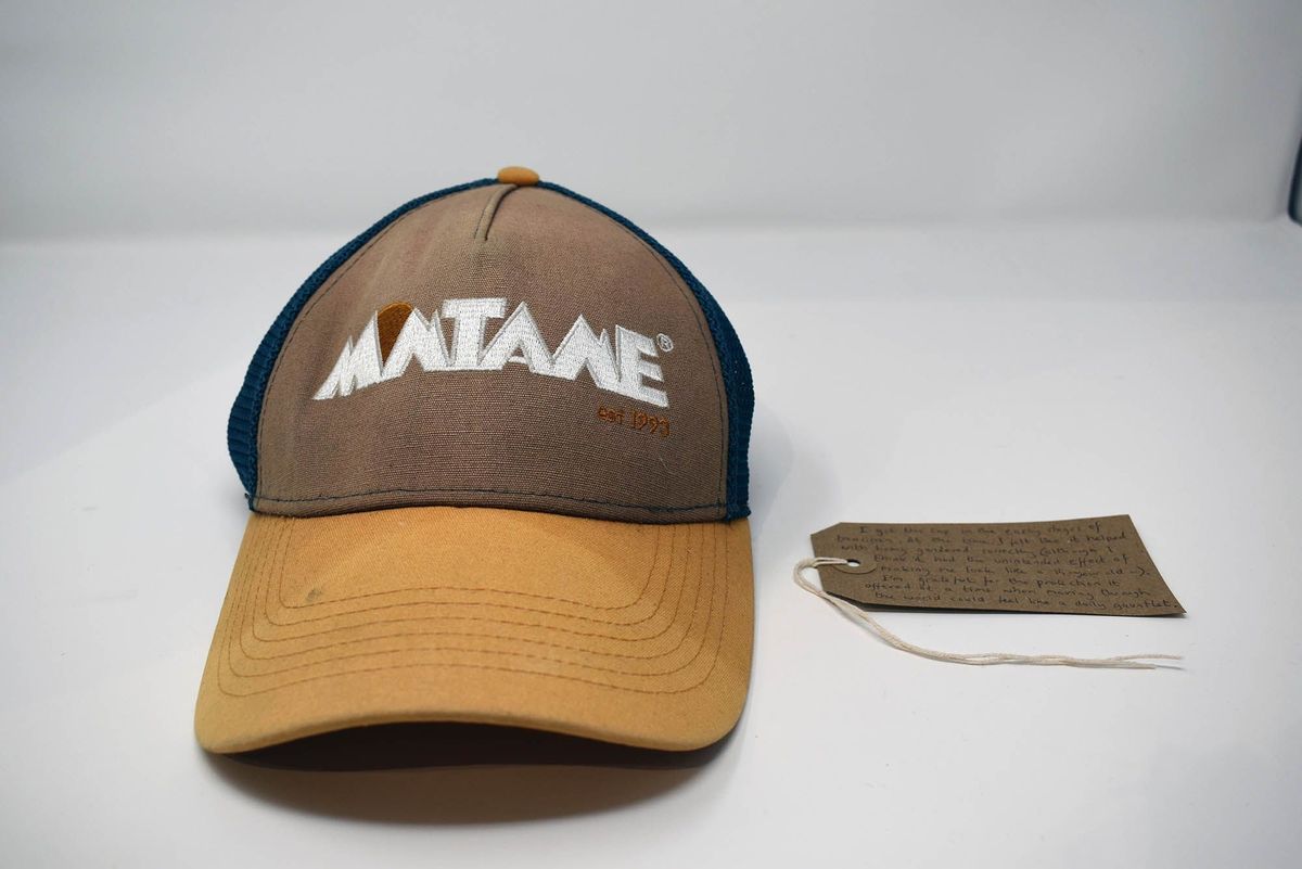 A brown and blue trucker hat displays "MATAKE" with a descriptive tag beside it.
