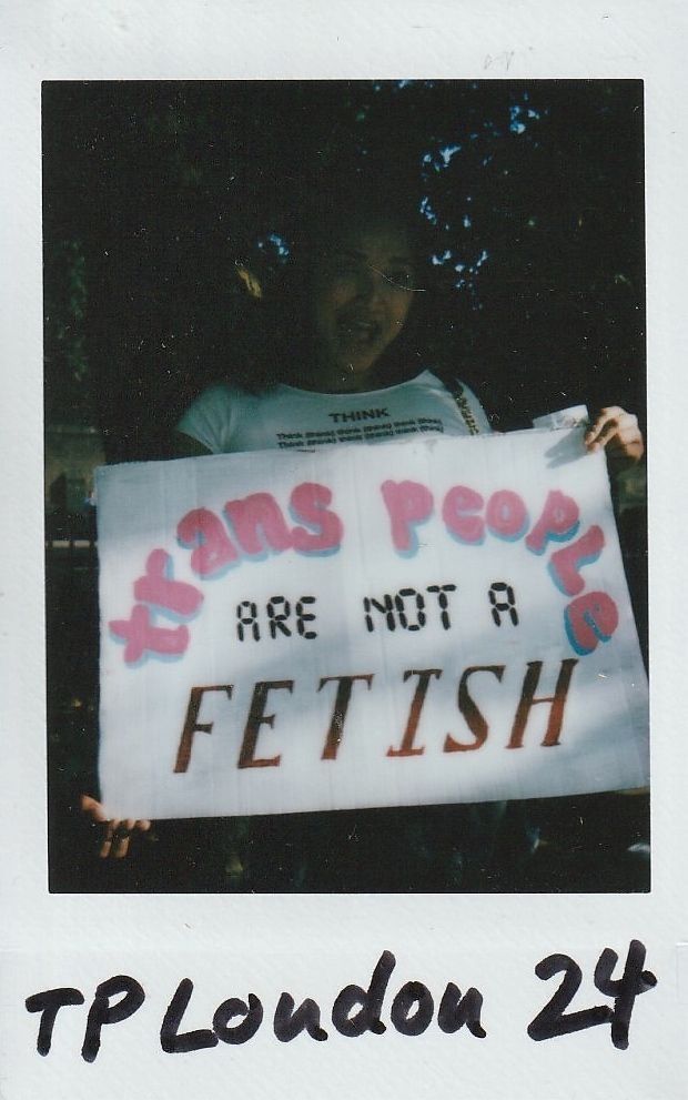 A person holds a sign stating, "Trans people are not a fetish," in the photograph.