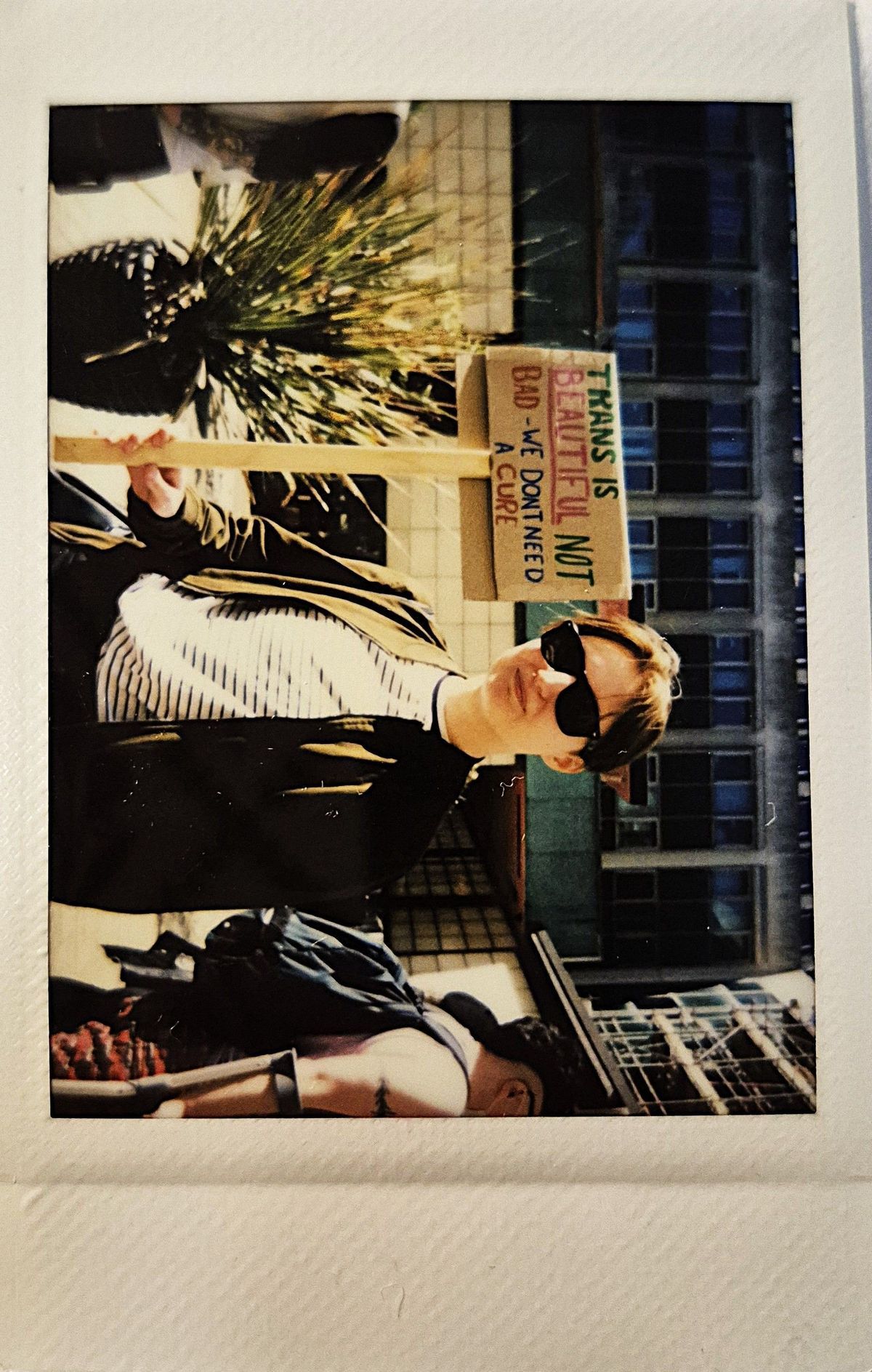 A person wearing sunglasses holds a sign stating "Trans is beautiful".