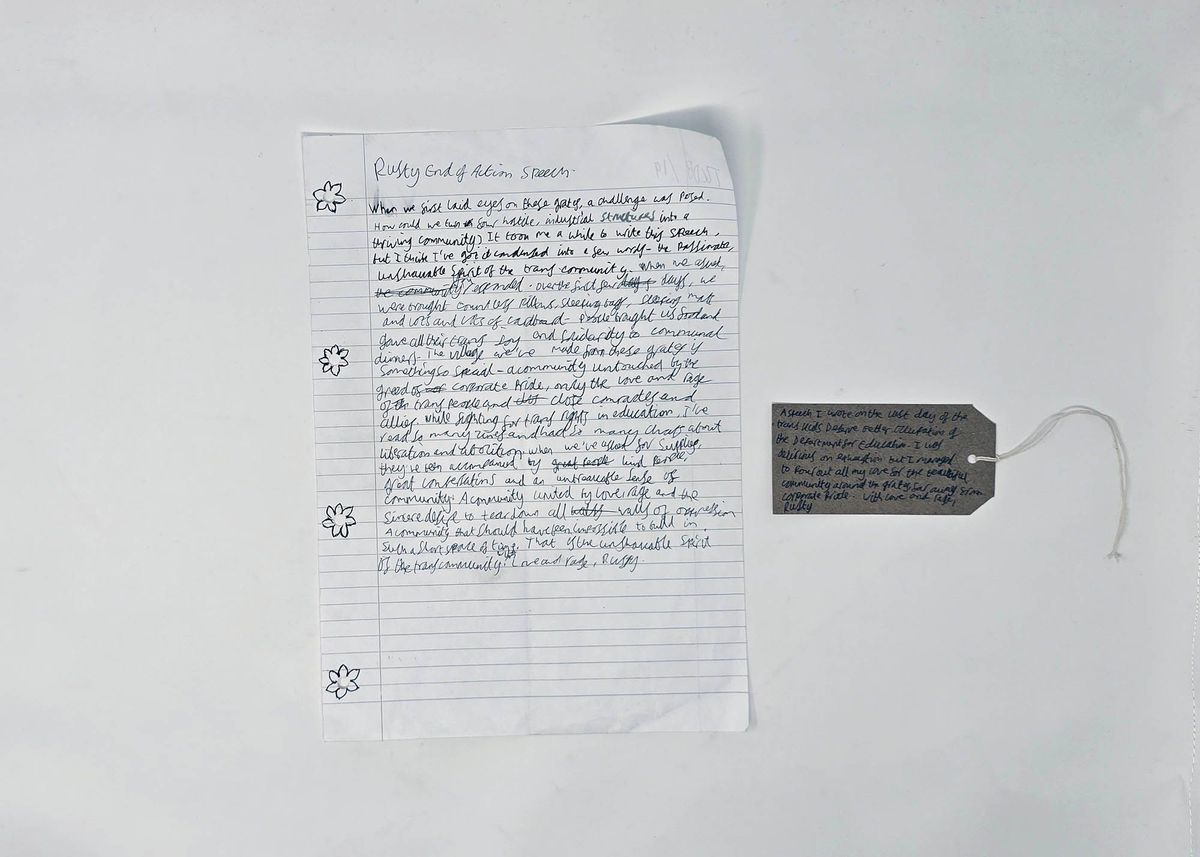 A sheet of lined A4 paper with the handwritten text of a speech, titled "Rusty end of Action Speech". It is written in black pen and there are flowers drawn around the punch holes in the left margin. With a brown, handwritten luggage tag.