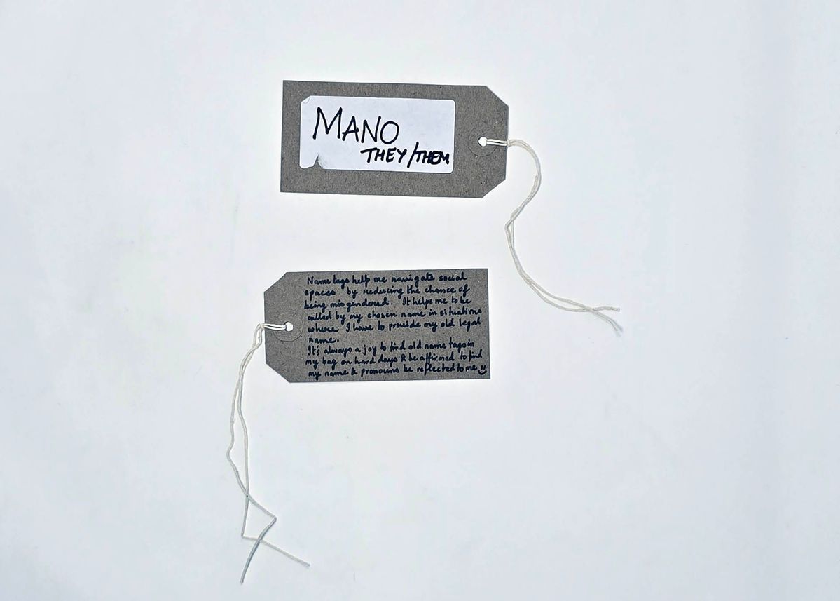 A handwritten name tag inscribed "MANO" "THEY/THEM". With a brown handwritten luggage tag.