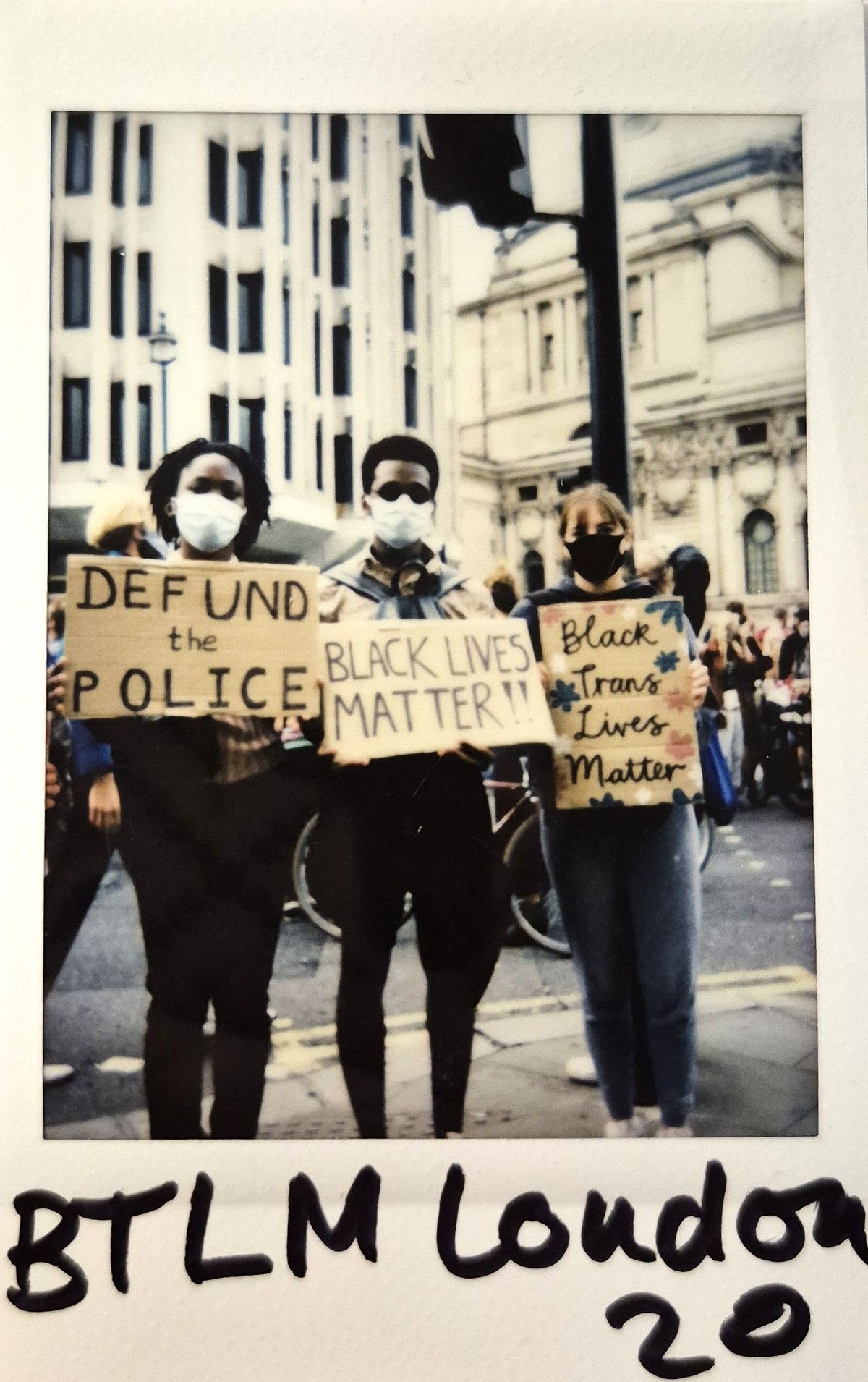 Three masked individuals hold protest signs supporting Black Lives Matter, standing outside.