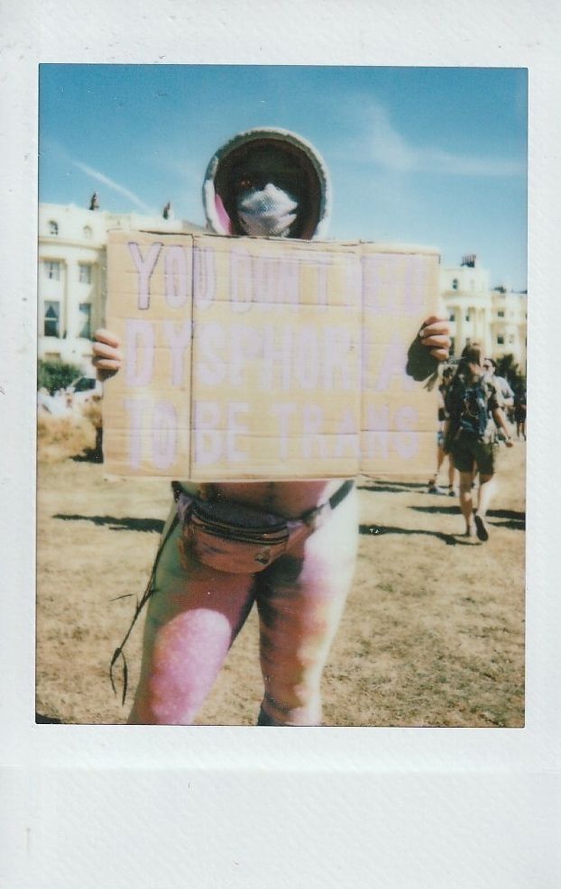 A person holds a sign reading "You don't need dysphoria to be trans".