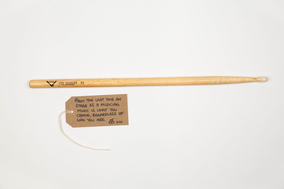 A drumstick with some small writing on it next to a brown tag with writing.