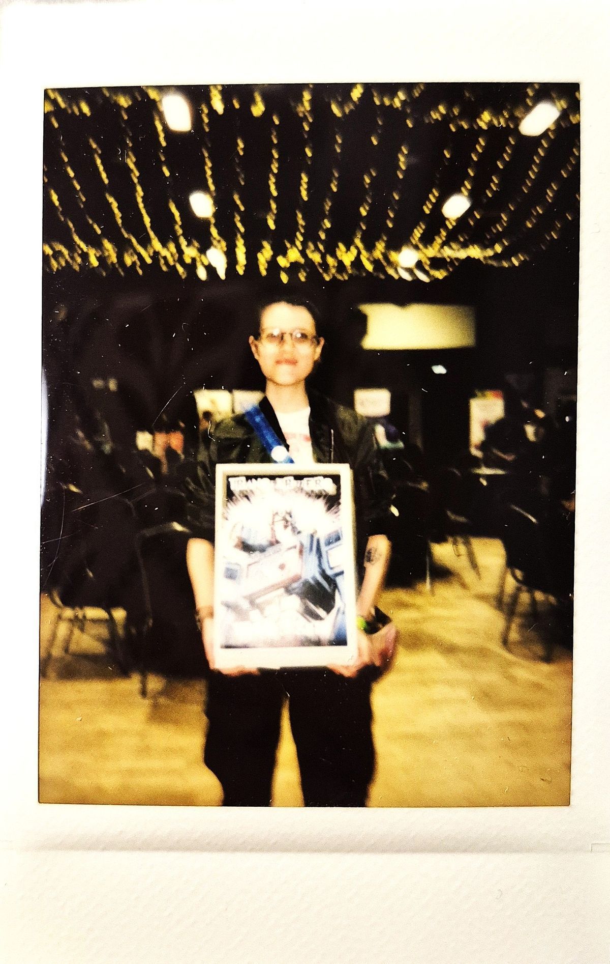 A person is holding a framed picture in a dimly lit room with string lights overhead.