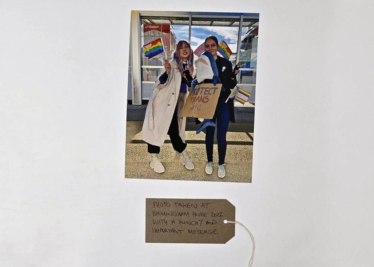 Photograph Showing Two People, One Holding A "PROTECT TRANS KIDS" Sign.