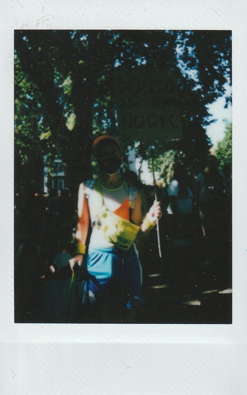 A person in bright clothing holds a sign amid a sunny outdoor setting with trees.