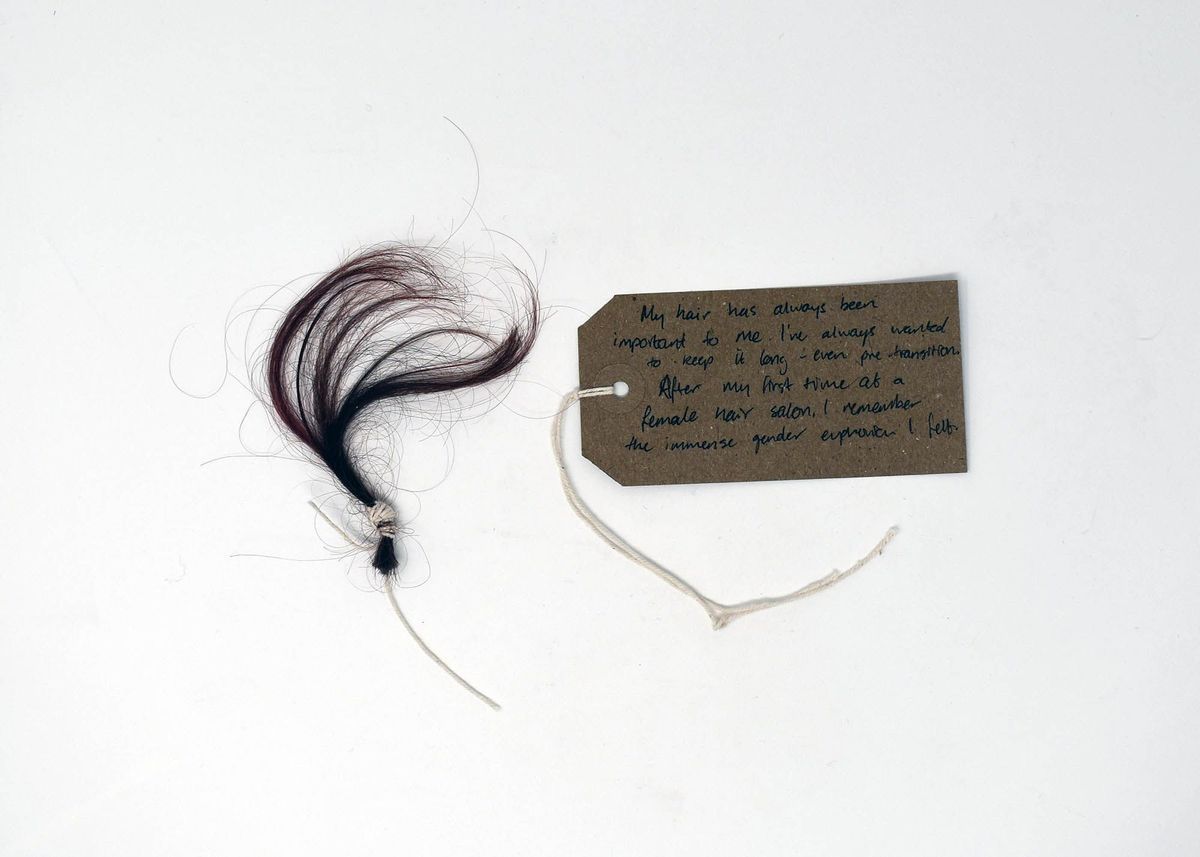 A small tuft of tied dark hair lies next to a handwritten tag on a string.