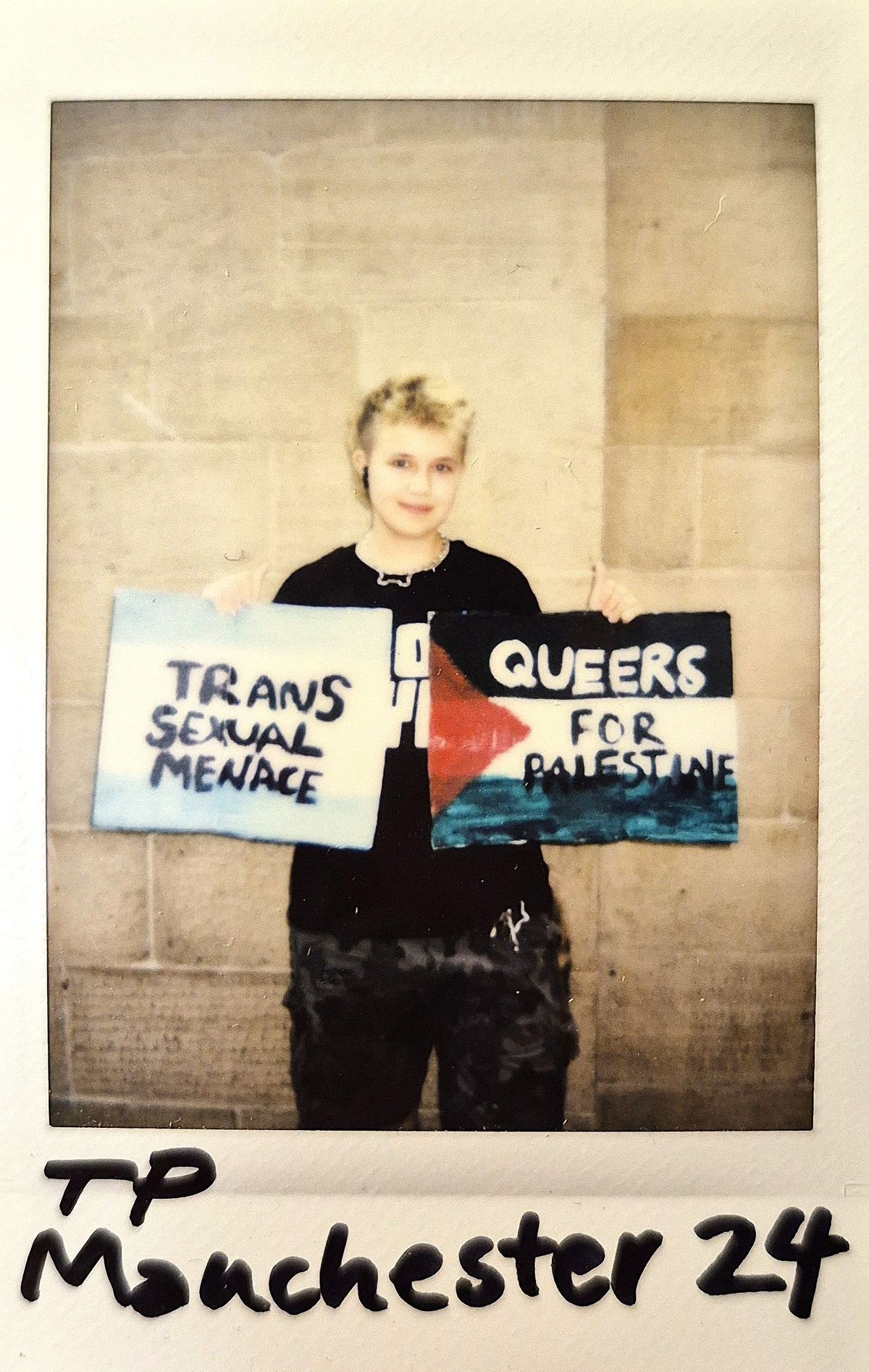 A person holds signs reading "Trans Sexual Menace" and "Queers for Palestine".