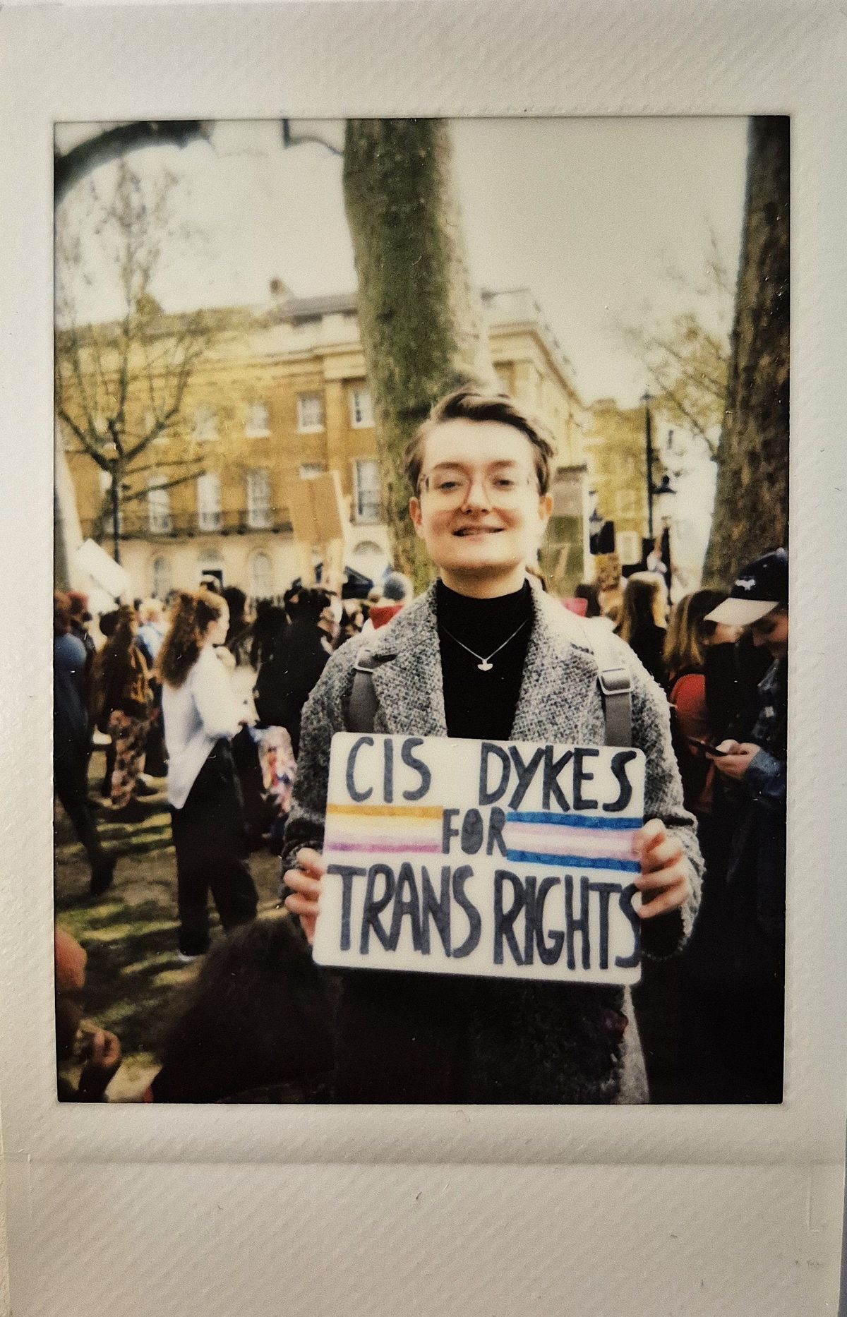 A person smiles while holding a sign which says "CIS DYKES FOR TRANS RIGHTS".