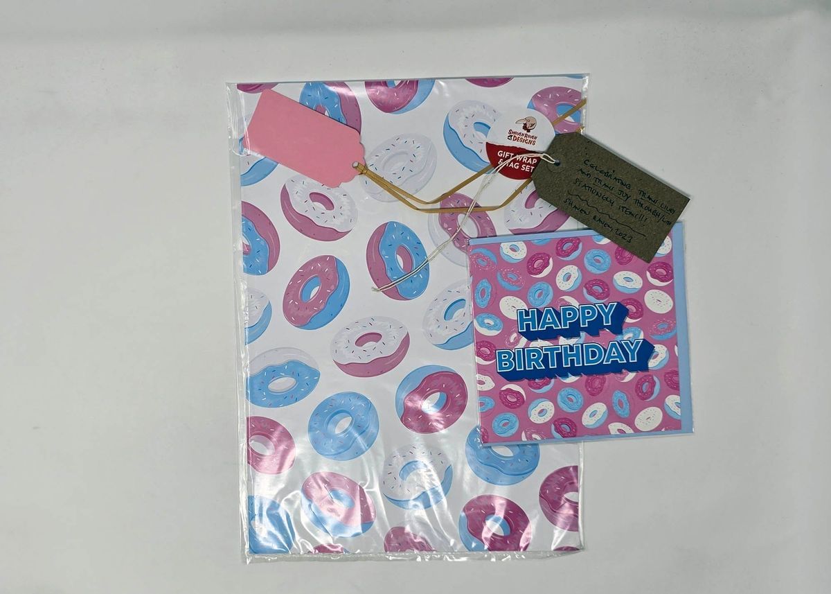 Matching gift wrap and birthday card illustrated with cartoon frosted donuts in pink, blue and white. With a brown, handwritten luggage tag.