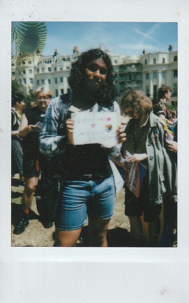 A person stands outdoors holding a sign while surrounded by others during a protest.