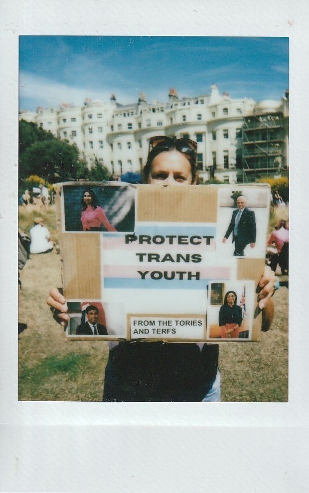 A person holds a sign which says "PROTECT TRANS YOUTH FROM THE TORIES AND TERFS".