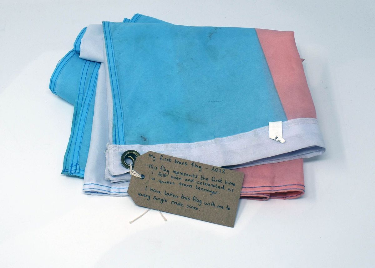 A slightly dirty from use folded up trans flag with a brown tag with writing on it attached.