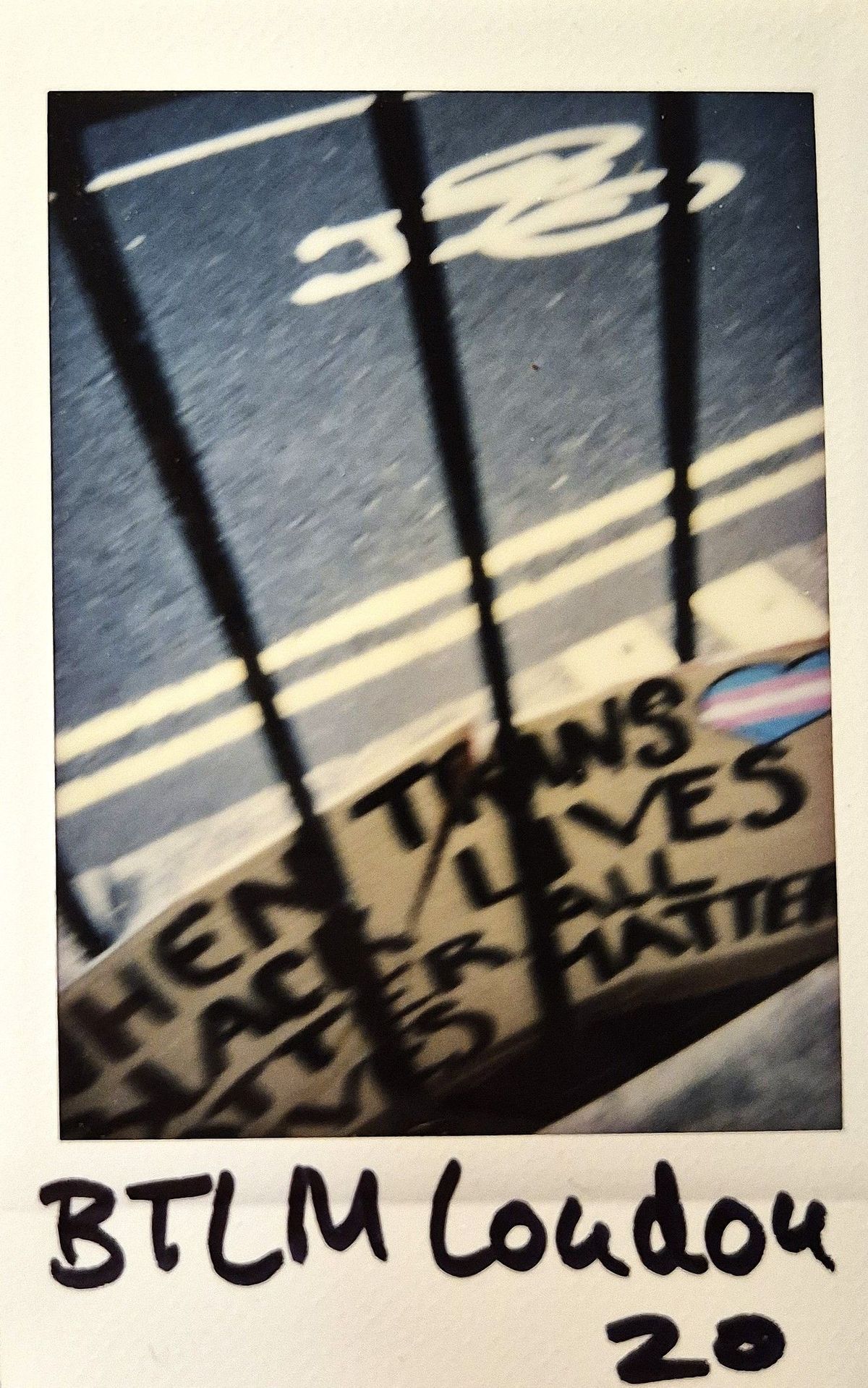 A blurry photo shows a street with signs and a trans flag heart, alongside “BTLM London".